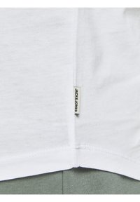Camiseta de algodón blanca con tejido liso, mangas cortas y una etiqueta lateral con el logotipo "JACK & JONES". Las costuras son visibles a lo largo del dobladillo.