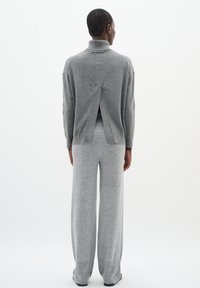 Gray knit pullover with high collar, featuring a back split; paired with wide-leg gray trousers, both made from soft fabric.