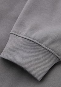 Grå sweatshirtärm med ribbad mudd, med en slät yta och jämn färg, som framhäver sömdetaljer längs sömmen.