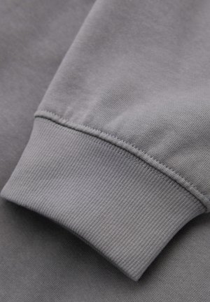 Hihnan harmaa collegepaida, jossa on ribbattu cuff, näyttäen sileää rakennetta ja tasaista väriä, korostaen ompelusaumojen yksityiskohtia.