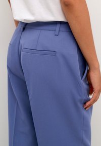 Světle modré tailored kalhoty s hladkou texturou, se dvěma zadními kapsami a bočními kapsami, strukturovaným střihem a poutkem na opasek.