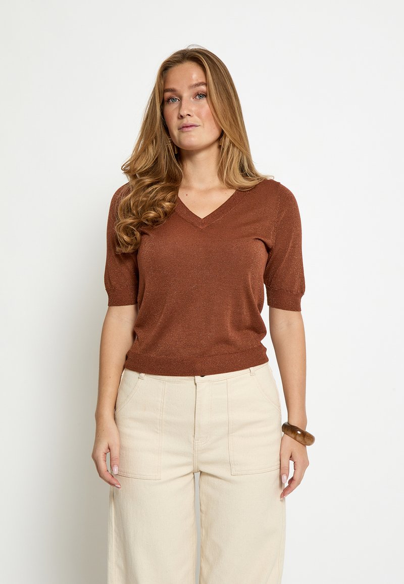 Bronzen V-hals trui met korte mouwen, geribde zoom en subtiele glans, gecombineerd met beige broek met wijde pijpen. Gladde textuur met een aansluitende pasvorm.