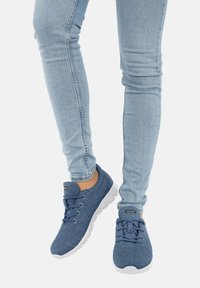 Blaue Stoff-Sneaker mit weicher Textur, weißer Gummisohle und Schnürdesign. Getragen mit hellblauen Skinny-Jeans.