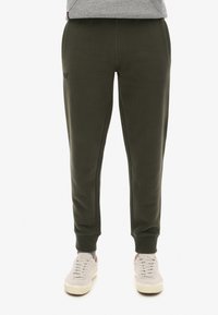 Olijfgroene sweatpants van zacht materiaal, met zijkisten, elastische boorden en een klein logo detail bij de tailleband.