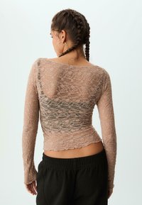 Langærmet bluse i lys pink med blonde, prydet med et blomster mønster og en let bølget kant. Bæres med sorte bukser med elastisk talje.