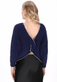 Donkerblauwe fuzzy gebreide trui met een diepe V-rug, voorzien van een geschulpte rand en losse, brede mouwen, gestyled over een zwarte aansluitende rok.