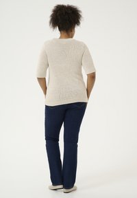 Pull en maille crème à manches courtes, associé à un jean slim bleu foncé. Le pull présente un col rond et un tissu texturé.