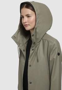 Water-resistant olive green rain jacket with a large hood, snap buttons, drawstrings, and a smooth, glossy finish.
