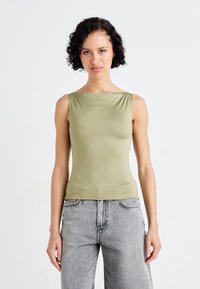 Olivgrön ärmlös topp i en mjuk, elastisk tyg med fyrkantig halsringning, kombinerad med ljusgrå, högmidjade jeans.