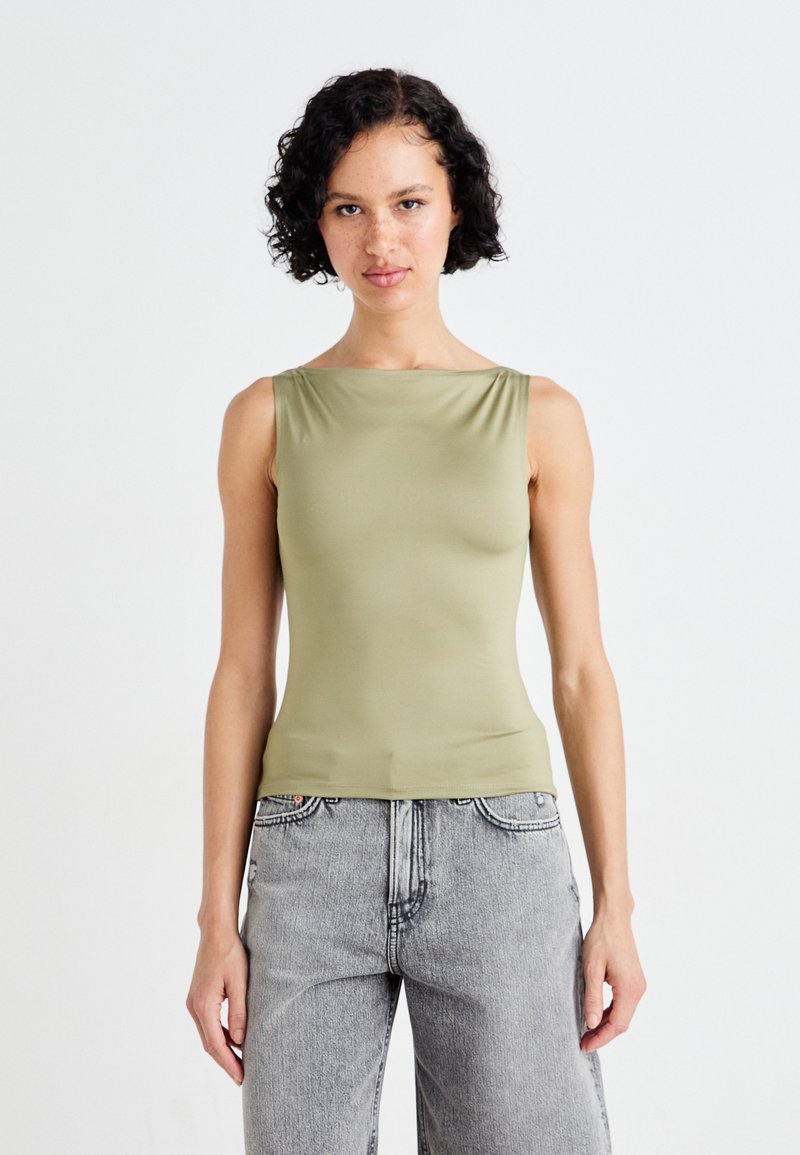 Olivgrön ärmlös topp i en mjuk, elastisk tyg med fyrkantig halsringning, kombinerad med ljusgrå, högmidjade jeans.
