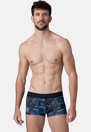 Vīriešu bokserbikses tumši zilā krāsā ar grafisku apdruku. Tās ir ar melnu jostu, uz kuras ir redzams zīmola nosaukums. Materiāls šķiet elastīgs un gluds.