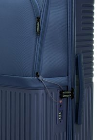 Valise bleu marine avec surface texturée, nervures verticales, double zip et verrou à combinaison intégré pour la sécurité. Étiquette de marque affichée.
