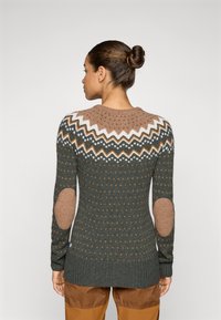 Knit sweater featuring a green base, brown patterned yoke, and elbow patches. Textured with vertical dots and a ribbed hem.