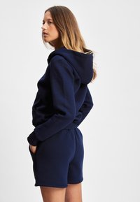 Marineblå hettegenser med elastiske mansjetter og lomme, kombinert med matchende marineblå shorts med elastisk midjebånd og sidelommer.