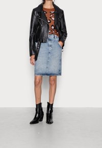 Czarna skórzana kurtka motocyklowa z elementami w kolorze srebrnym, zestawiona z brązowym swetrem w zwierzęcy wzór i jasnoniebieską dżinsową ołówkową spódnicą. Czarne botki za kostkę.