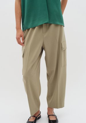 Beige cargo pants with side pockets, relaxed fit, soft texture, and a straight cut. Worn with a green top and black flats.