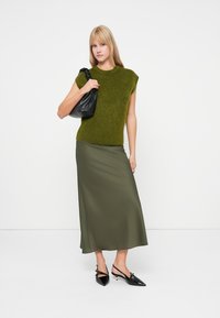 Olívovo zelené tričko s krátkym rukávom z chlpatého úpletu v kombinácii s dlhou olivovou saténovou sukňou. Doplnky zahŕňajú čiernu koženú tašku a lesklé čierne lodičky.