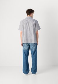 Kortermet, lyseblå stripete skjorte med rett passform, kombinert med løstsittende lyseblå jeans og hvite sneakers.