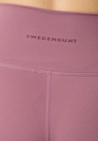 Højtaljede leggings i lys lilla, lavet af glat stof. Har syninger og brandnavnet "SWEDEMOUNT" i lilla ved taljen.
