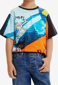 Kortærmet skjorte med et farverigt print i graffiti-stil i blå, orange og sort. Har grafiske designs og en ribbet rund halsudskæring.