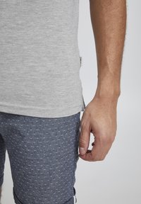 Lys grå bomulls t-skjorte med rund fald og sideslit, kombinert med mørkeblå mønstrede shorts med små diamantformer.