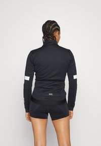 Svart sportjacka med hög krage, reflekterande vita detaljer på ärmarna och en åtsittande design. Bärs med matchande shorts.