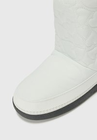Witte gewatteerde laars met een ronde neus en een glad bovenwerk. Beschikt over een grijze rubberen zool en contrasterende stiksels langs de rand.