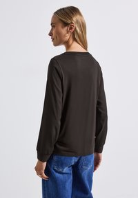 Schwarzes Langarmoberteil mit lockerer Passform und gerippten Bündchen, kombiniert mit blauen Denim-Jeans. Der Stoff hat eine glatte Textur und ein einfaches Design.