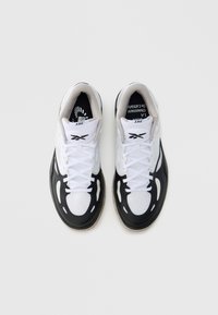 Czarno-białe buty sportowe z cholewką wykonaną z różnych materiałów, zaokrąglonym noskiem, białymi sznurowadłami oraz teksturowaną podeszwą z widocznymi rowkami.