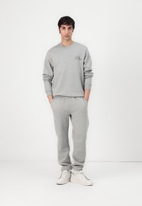 Hanorac gri și pantaloni de trening asortați, dintr-un material moale. Hanoracul are un logo mic verde; ținuta este completată cu adidași albi.