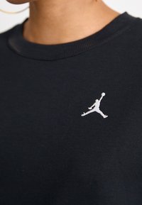 Sudadera negra de algodón con cuello redondo, que presenta un logo Jumpman bordado en blanco en el pecho. Textura suave, diseño simple.