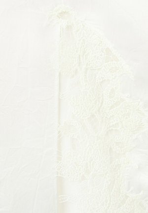 Tissu blanc transparent avec un détail en dentelle florale délicate le long d'un bord, montrant des motifs raffinés et une texture fine.