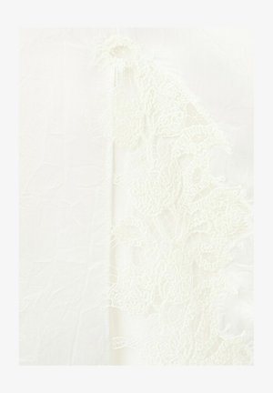 Tela blanca transparente con detalle intrincado de encaje floral a lo largo de un borde, mostrando patrones delicados y textura fina.