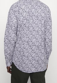 Pitkähihaisessa paidassa on kevyt kangas, valkoinen ja tummansininen pilkullinen kuvio, kaareva helma ja napitettava kaulus.