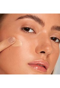 Lightweight, creamy foundation being applied to textured, warm-toned skin. Natural finish, with a focus on smoothness and even color.