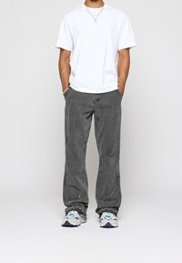 Harmaat farkut, joissa on rento istuvuus, sivuvetoketjut ja ompelusarjat, yhdistettynä valkoiseen T-paitaan ja monivärisiin lenkkareihin.