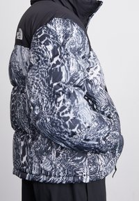 Dunjakke med sort overdel og et tekstureret gråt og hvidt abstrakt mønster. Har lynlåslukning og elastiske manchetter. Varm og isolerende design.