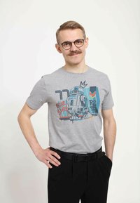 Camiseta de algodón gris con un diseño estilizado de R2-D2 y acentos de colores, combinada con pantalones negros y un cinturón negro.