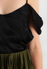 Top in satin nero con una vestibilità ampia e un'unica spallina, abbinato a una gonna plissettata verde oliva. Texture liscia e drappeggio elegante.