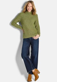 Grüner Strickpullover mit geripptem Kragen und Saum, kombiniert mit dunklen Denim-weit Bein-Jeans und beigen Wildleder-Ankle Boots.