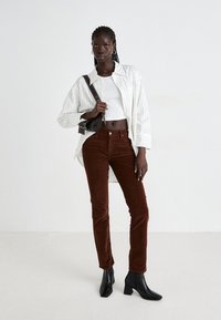 Bruine corduroy broek gecombineerd met een wit gestreept shirt over een witte crop top. Zwarte enkellaarsjes maken de outfit compleet. Eenvoudige handtas inbegrepen.