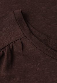 Gros plan d'un tissu côtelé marron foncé avec un col rond et un détail de couture froncée près de la couture de l'épaule.