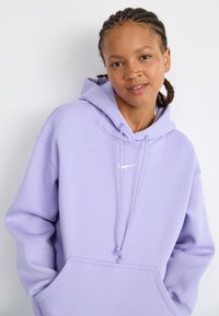 Hoodie roxo feito de um tecido macio, com um bolso frontal, capuz com cordão e um pequeno logotipo branco no peito. Ajuste ligeiramente oversized.