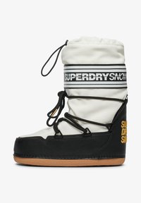 Botte de ski avec une tige blanche imperméable, une semelle en caoutchouc noir, des lacets réglables et un marquage bien visible en noir et jaune.