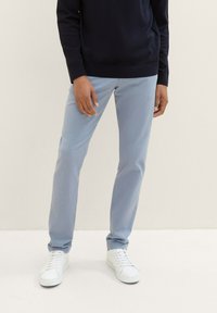 Light blue pants with a slim fit, featuring a smooth texture and subtle sheen. Paired with white sneakers and a dark sweater.