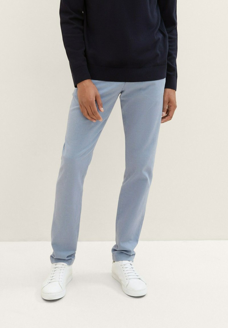 Light blue pants with a slim fit, featuring a smooth texture and subtle sheen. Paired with white sneakers and a dark sweater.