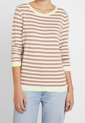 Mujer con camisa de manga larga de rayas horizontales beige y blancas con ribete verde claro combinada con vaqueros azul claro.