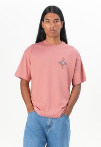 Light pink cotton t-shirt with a crew neck and short sleeves, featuring an embroidered design on the left chest and a relaxed fit.