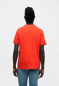 Czerwona bawełniana koszulka z okrągłym dekoltem i krótkimi rękawami, widziana od tyłu. Dopasowany krój z płaskimi szwami i gładką fakturą.