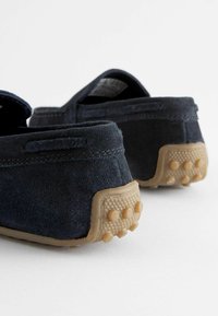 Marineblaue Wildleder Slipper mit einer strukturierten, tanfarbenen Gummisohle, die über kleine Griffpunkte verfügt und ein einfaches Design aufweist. Die Rückansicht hebt das weiche Material hervor.